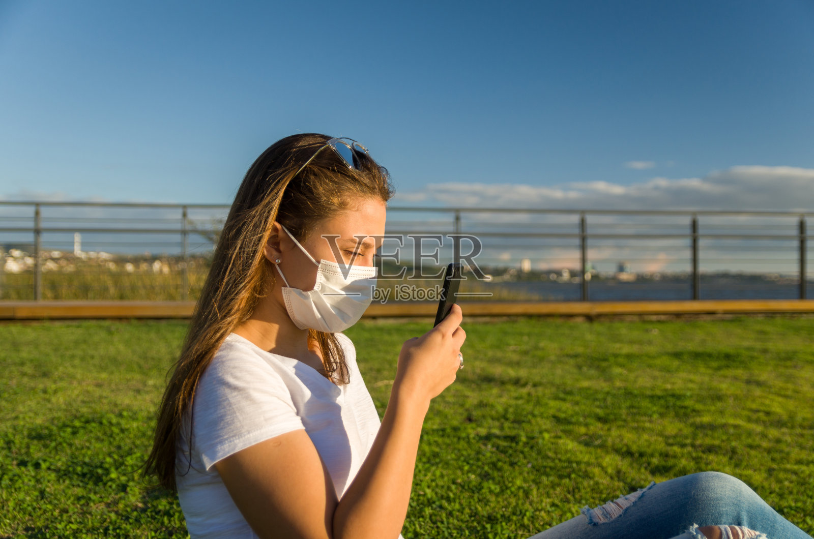 在SARS CoV-2大流行季节(COVID - 19)，年轻女子戴着防护口罩坐在草地上照片摄影图片