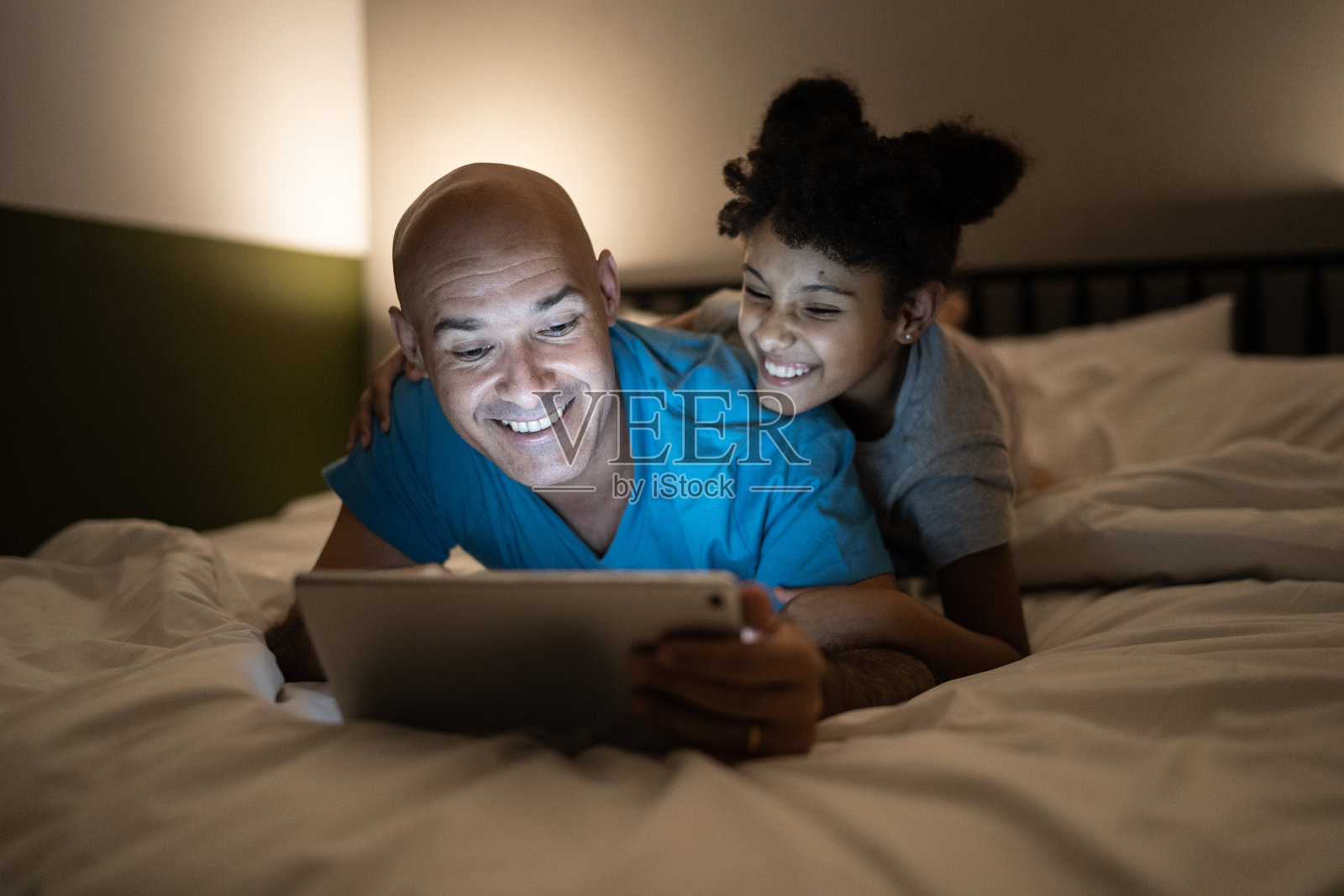父亲和女儿在床上看在家里使用数字平板电脑照片摄影图片