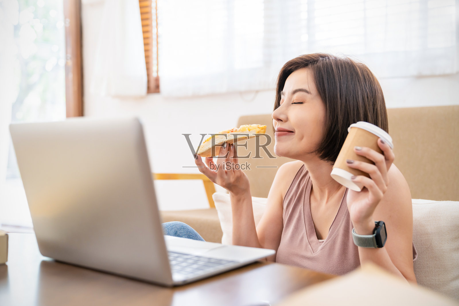 快乐的亚洲女性在笔记本电脑上工作，午休时间在沙发客厅上网吃披萨。送货，居家隔离工作新常态与拷贝空间背景照片摄影图片