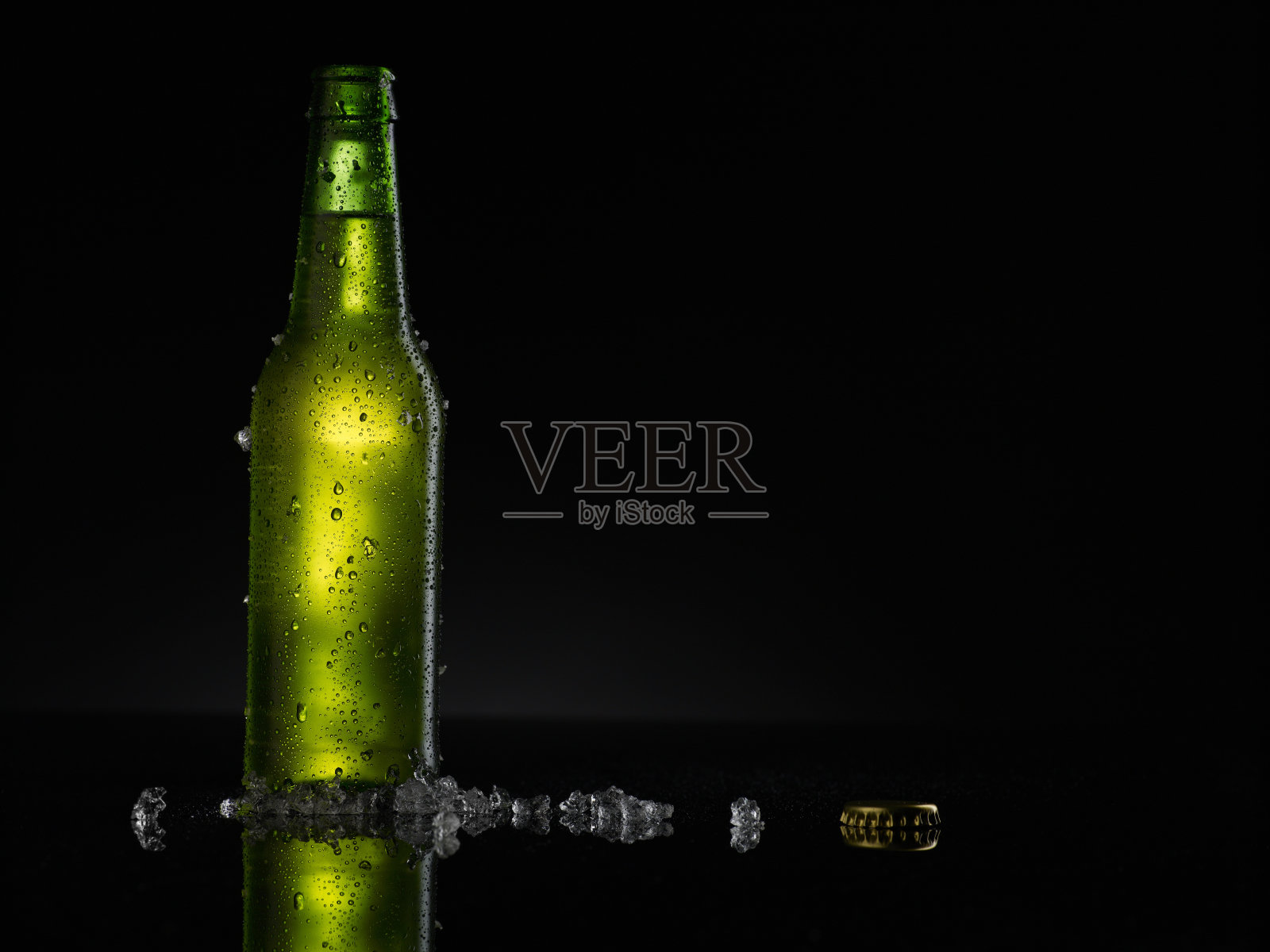 冰冷的绿色啤酒瓶上覆盖着水滴-凝结。空白饮料饮料产品设计模型。站在黑色的桌子上，黑色的背景。照片摄影图片