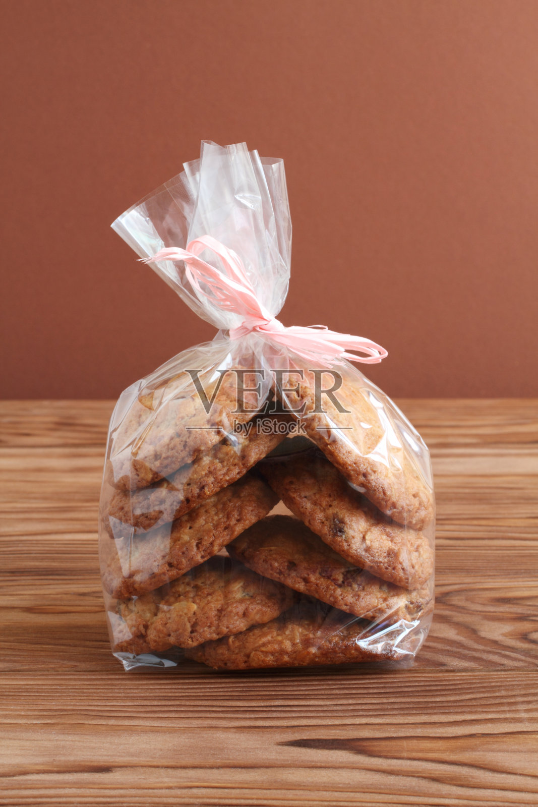 靠褐色墙壁的木桌上放着透明袋子里的燕麦饼干和蔓越莓干。特写镜头。宏照片摄影图片