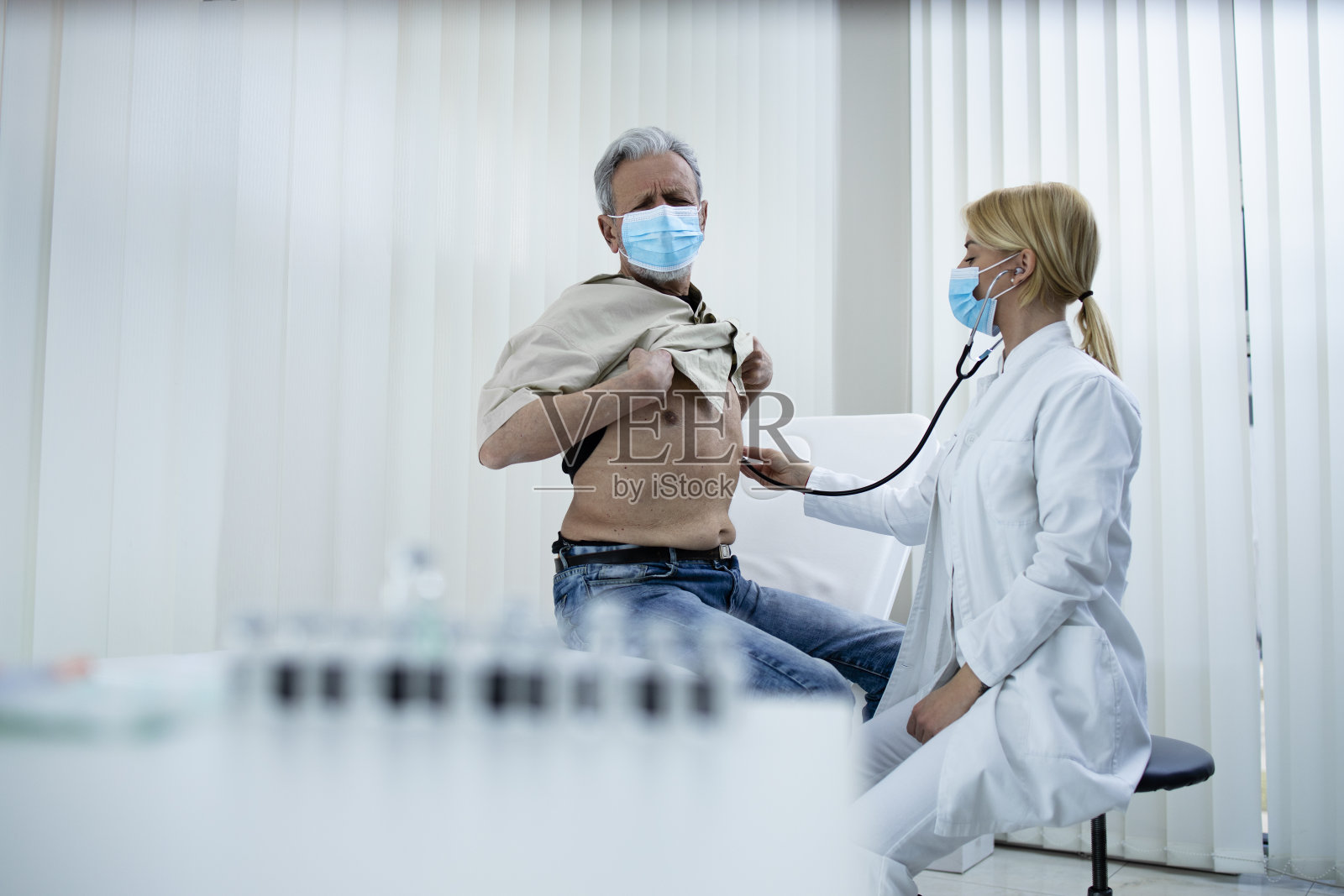 冠状病毒大流行期间，医生在医院办公室用听诊器检查老人的呼吸系统和肺部。照片摄影图片