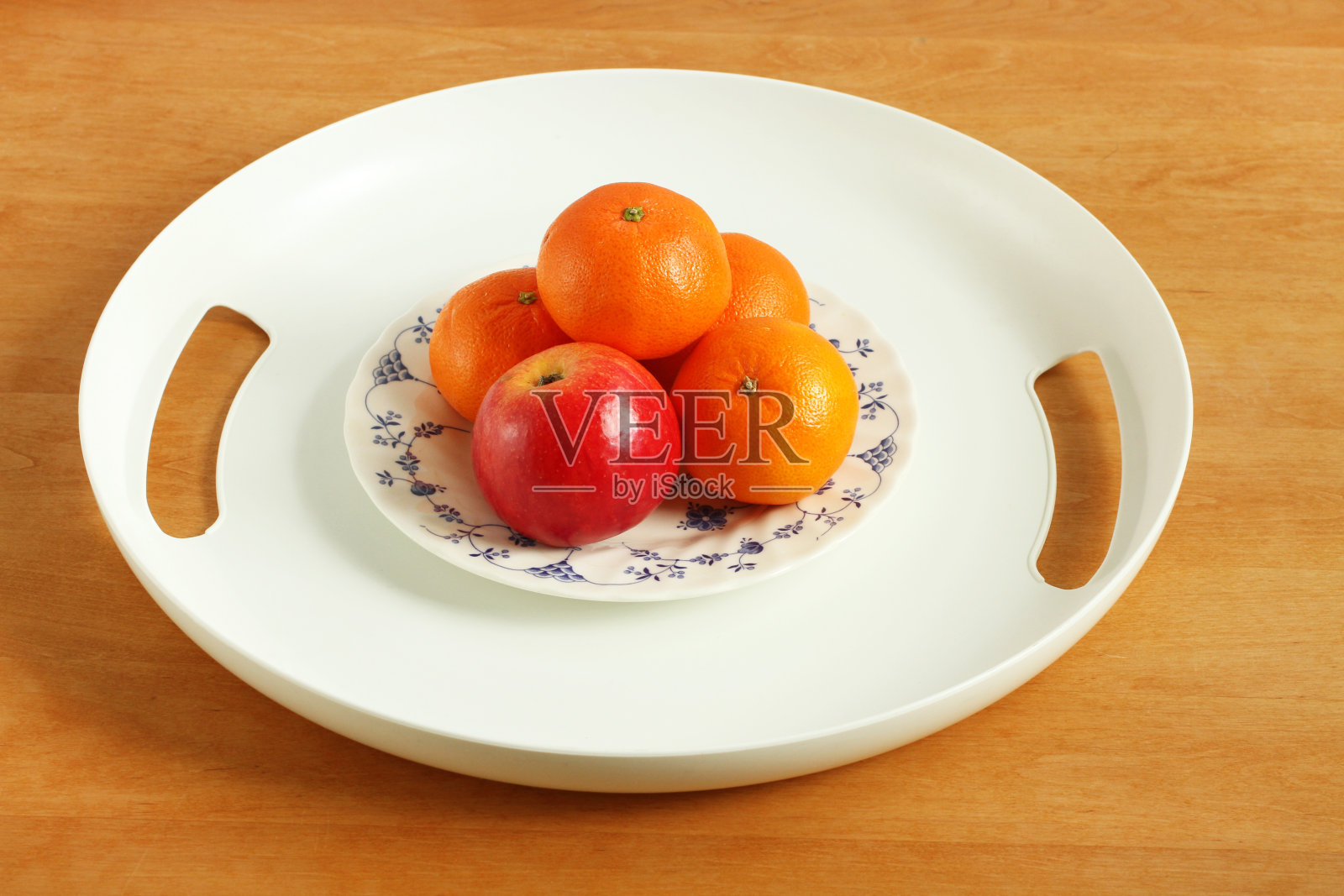 一个白色的塑料托盘，里面装着苹果和橘子，放在一张木桌上。照片摄影图片
