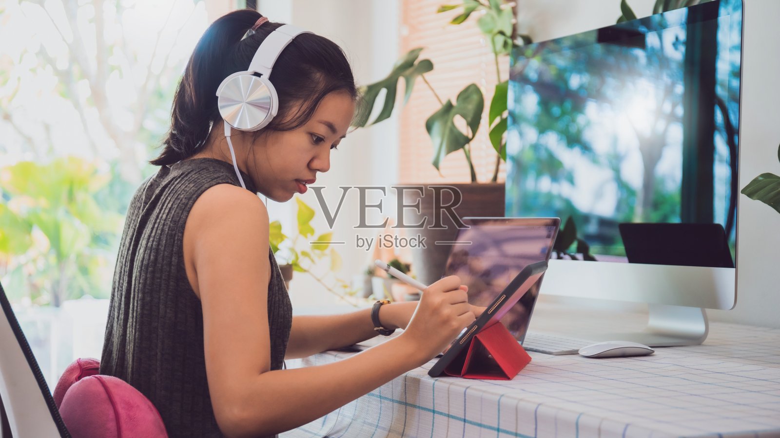 亚洲商务女性在家工作，桌上放着笔记本电脑、平板电脑和电脑，还有耳机。社会距离的概念是阻止冠状病毒疾病传播的感染控制行动。照片摄影图片
