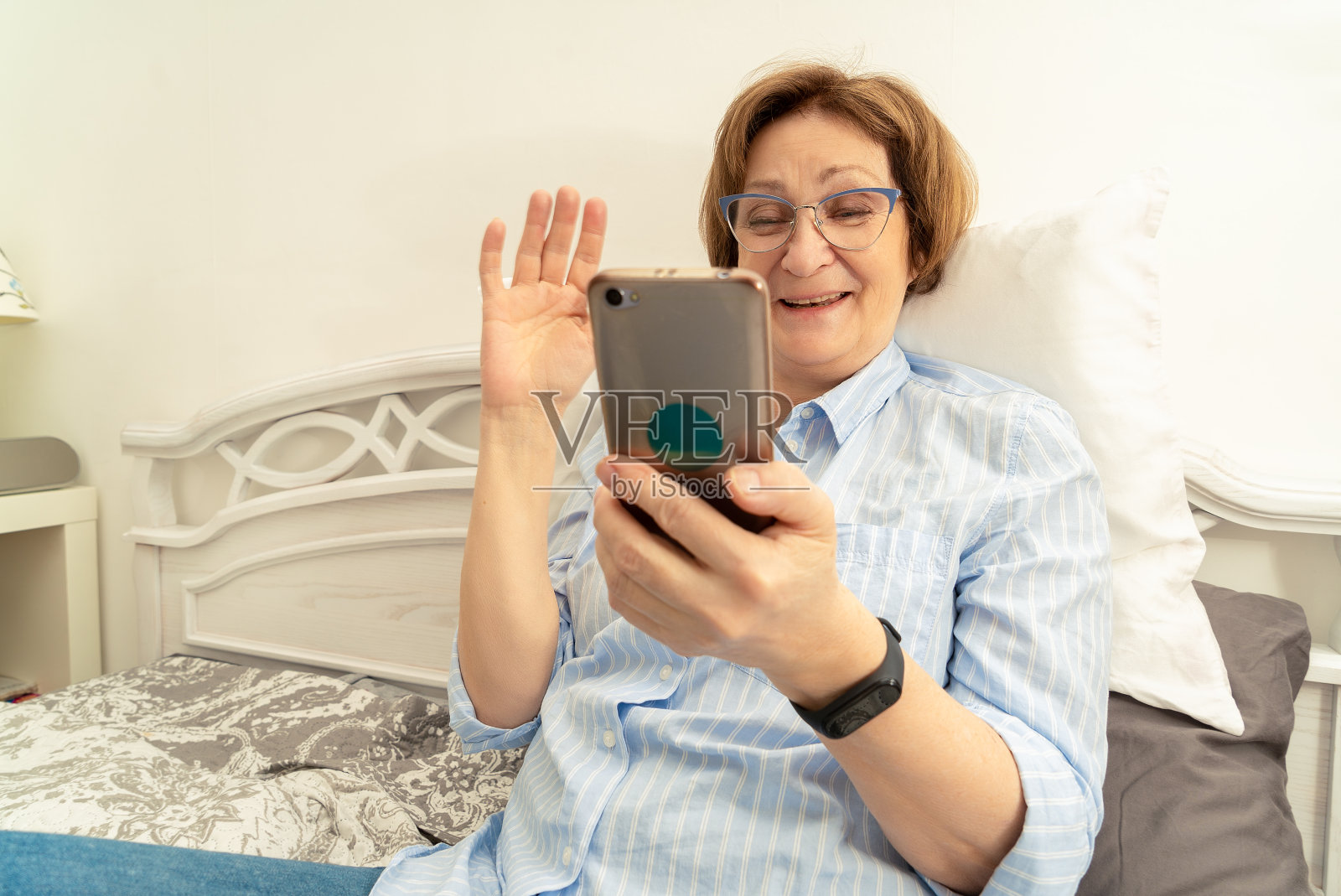 戴眼镜的老妇人用手机视频通话，愉快地表达问候照片摄影图片