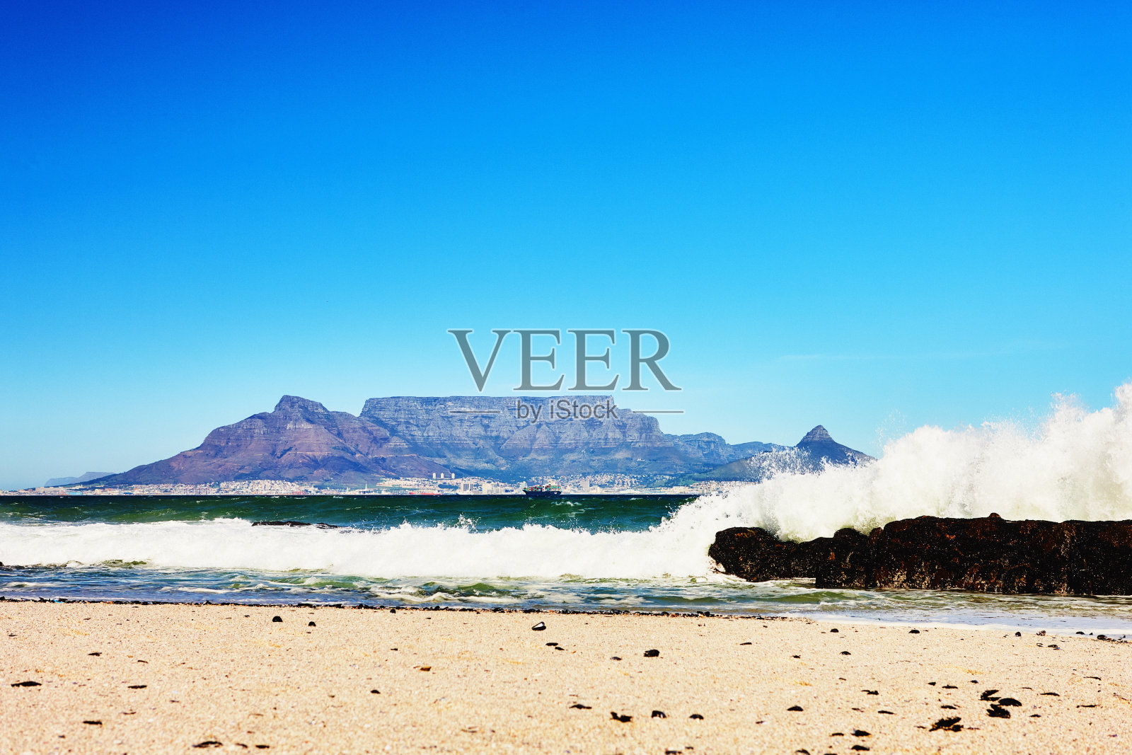 南非开普敦的桌山，从桌湾对面看到海浪拍打着岩石海岸照片摄影图片