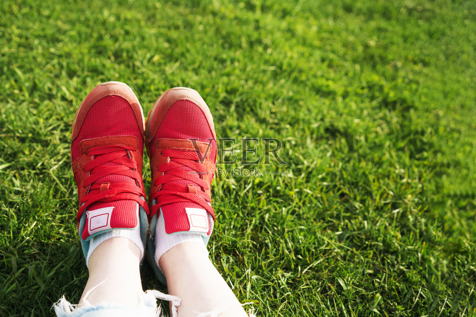 女人坐在草地上，女性的腿在绿色的草地上穿着红色的运动鞋照片摄影图片