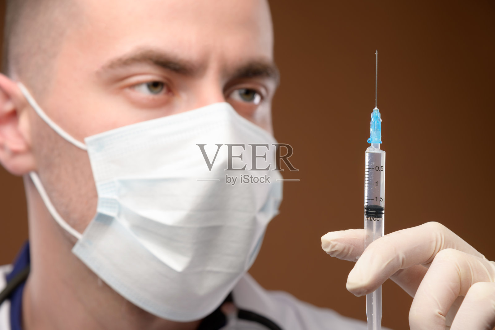 一名年轻的白人男性医生戴着面罩，用戴着手套的手拿着注射器进行注射。疫苗和疫苗注射概念。专注于注射器照片摄影图片