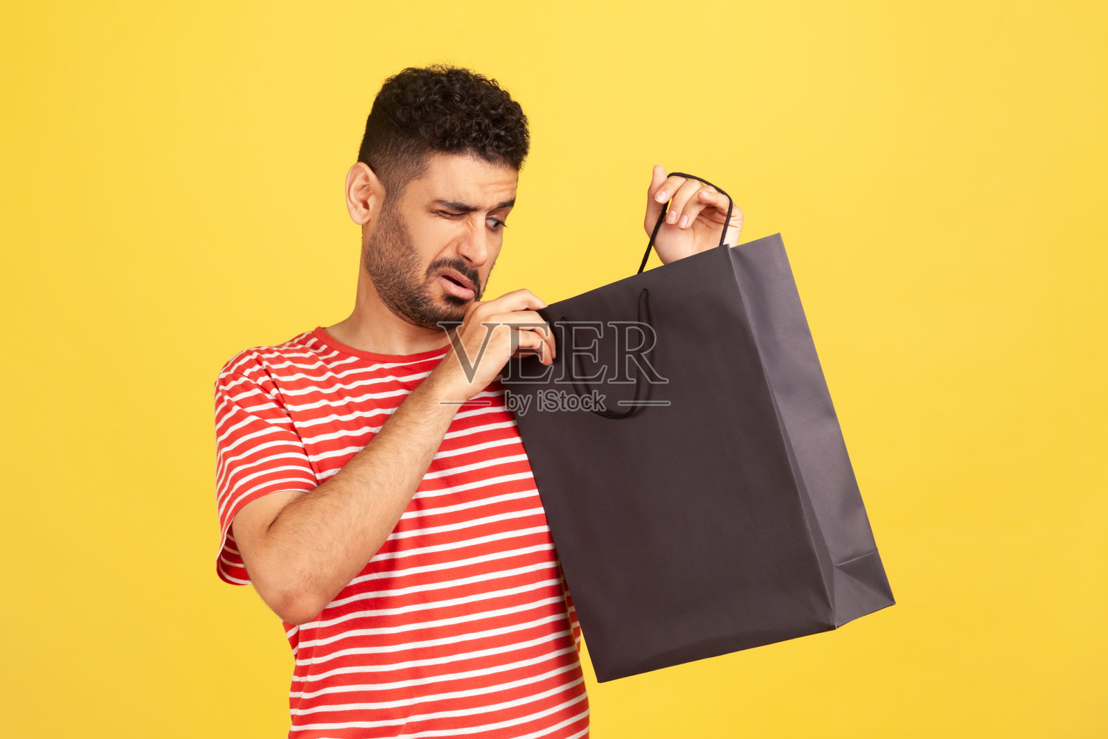一名穿着条纹t恤、留着胡子的好奇爱管闲事的男子，偷看着黑色的购物纸袋，打开礼物，试图猜测里面是什么，准备惊喜照片摄影图片