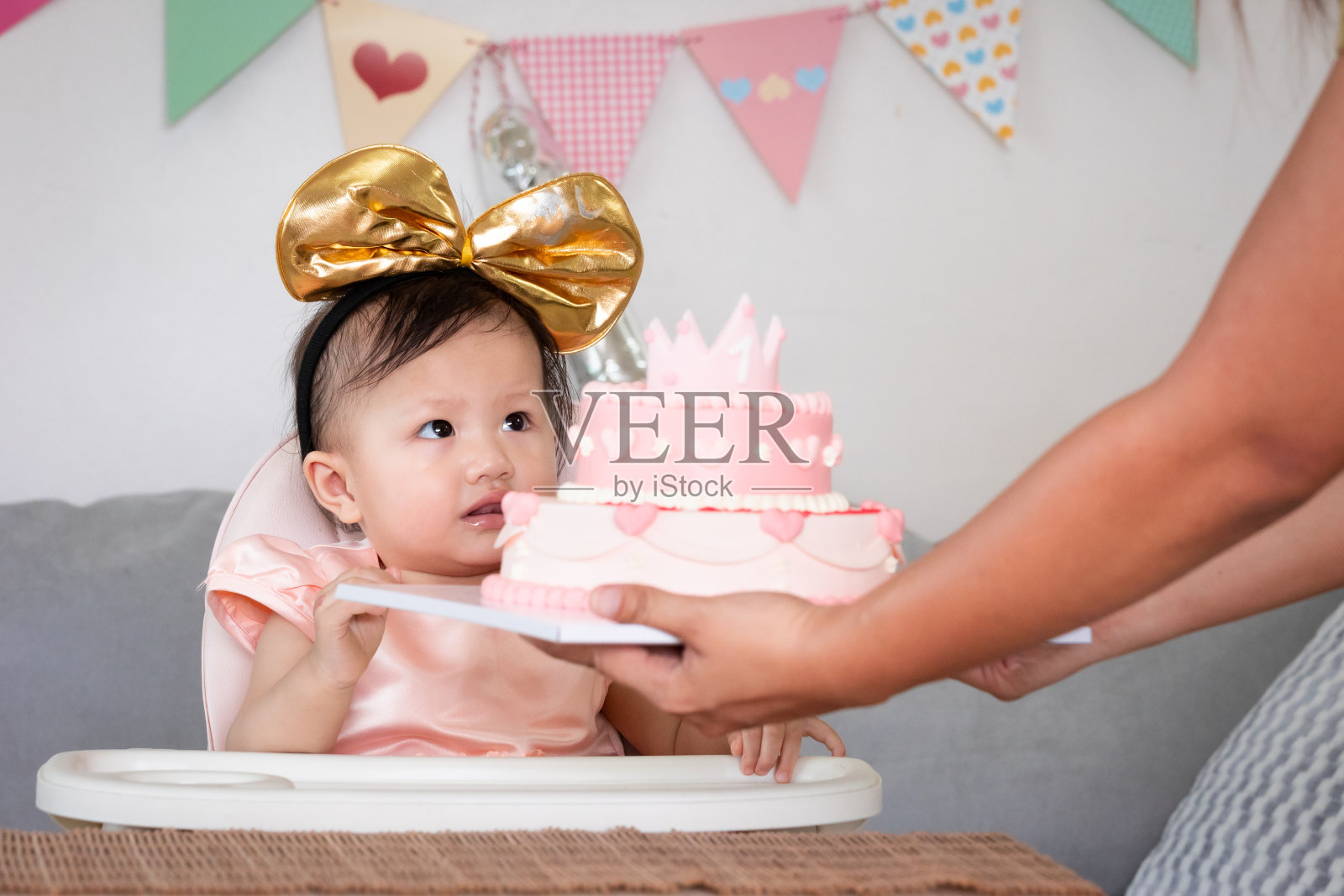 可爱的亚洲小女孩用粉红色公主蛋糕庆祝她的第一个生日。父母把生日蛋糕送给她可爱的女儿庆祝她的一岁生日。照片摄影图片