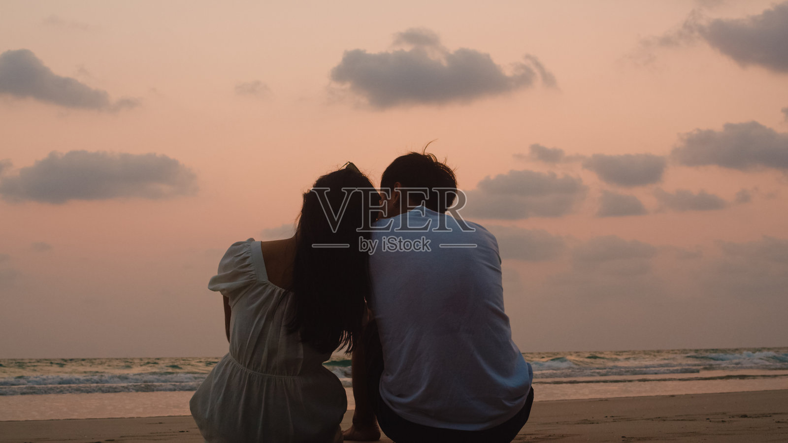 爸爸、妈妈和孩子坐在海边，拥抱放松一起看剪影日落。照片摄影图片