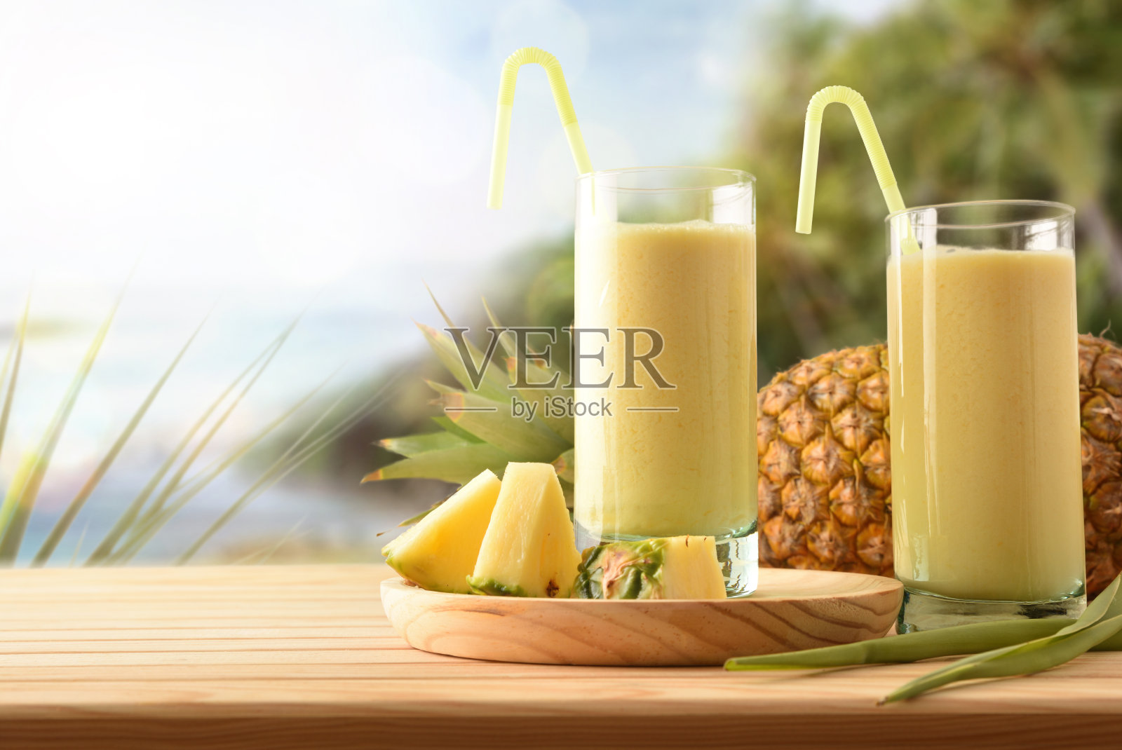 带有牛奶和热带海岸背景的菠萝汁玻璃杯照片摄影图片