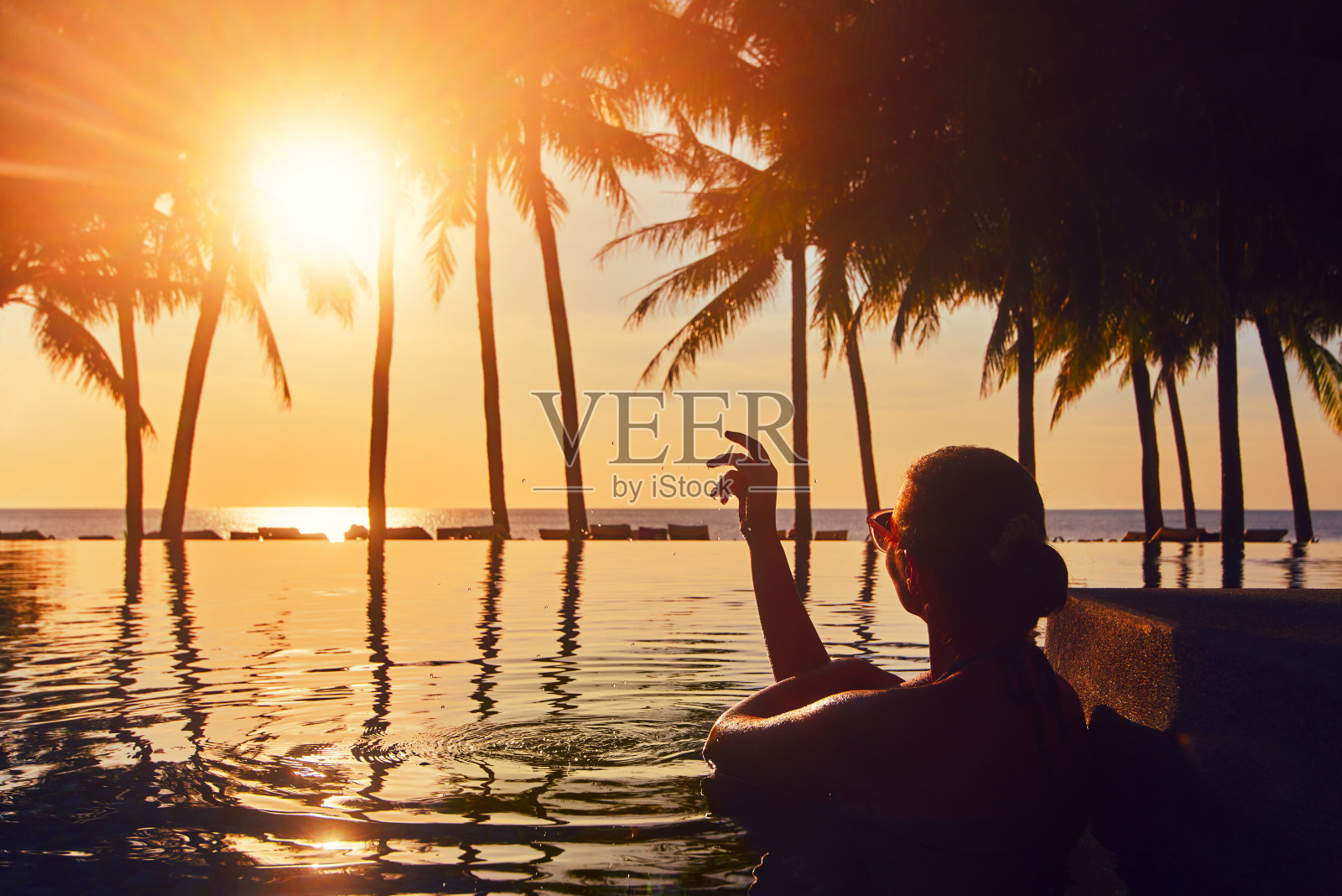 度假海滩夏季度假概念。剪影女子放松在游泳池在夏季海滩度假观看日落。照片摄影图片