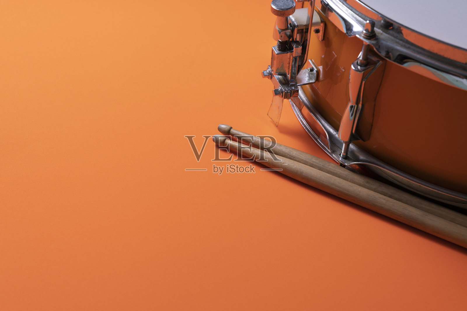 鼓棍和鼓在橙色的桌子上作背景，拉近了音乐的概念照片摄影图片