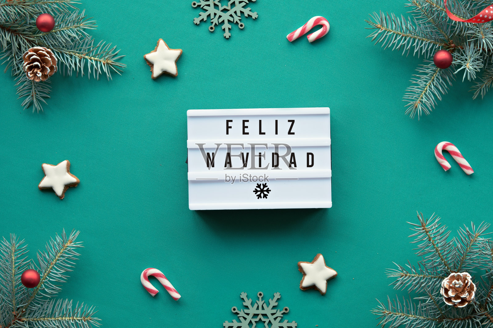 灯箱与文本Feliz Navidad -圣诞快乐在西班牙语。圣诞背景，顶视图冷杉树枝装饰红色玻璃小玩意，玩具，装饰在充满活力的绿松石纺织品照片摄影图片