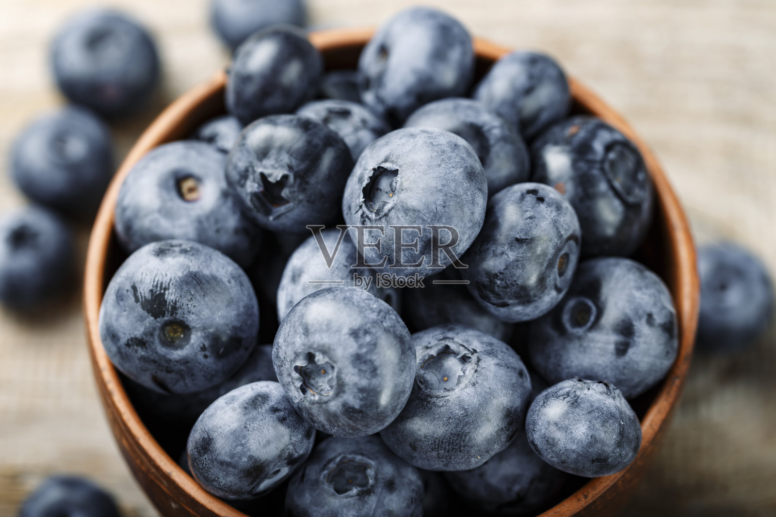 新鲜的蓝莓放在泥碗里，散落在木桌上。食物含有抗氧化剂。照片摄影图片