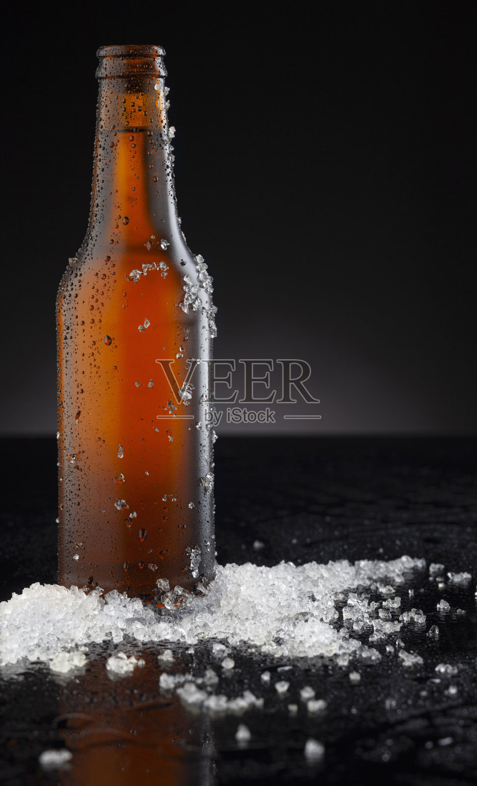 冰镇的棕色啤酒瓶覆盖着冰和水滴-凝结。用于饮料饮料产品设计模型的毛坯。站在黑色背景的黑色桌子上。照片摄影图片
