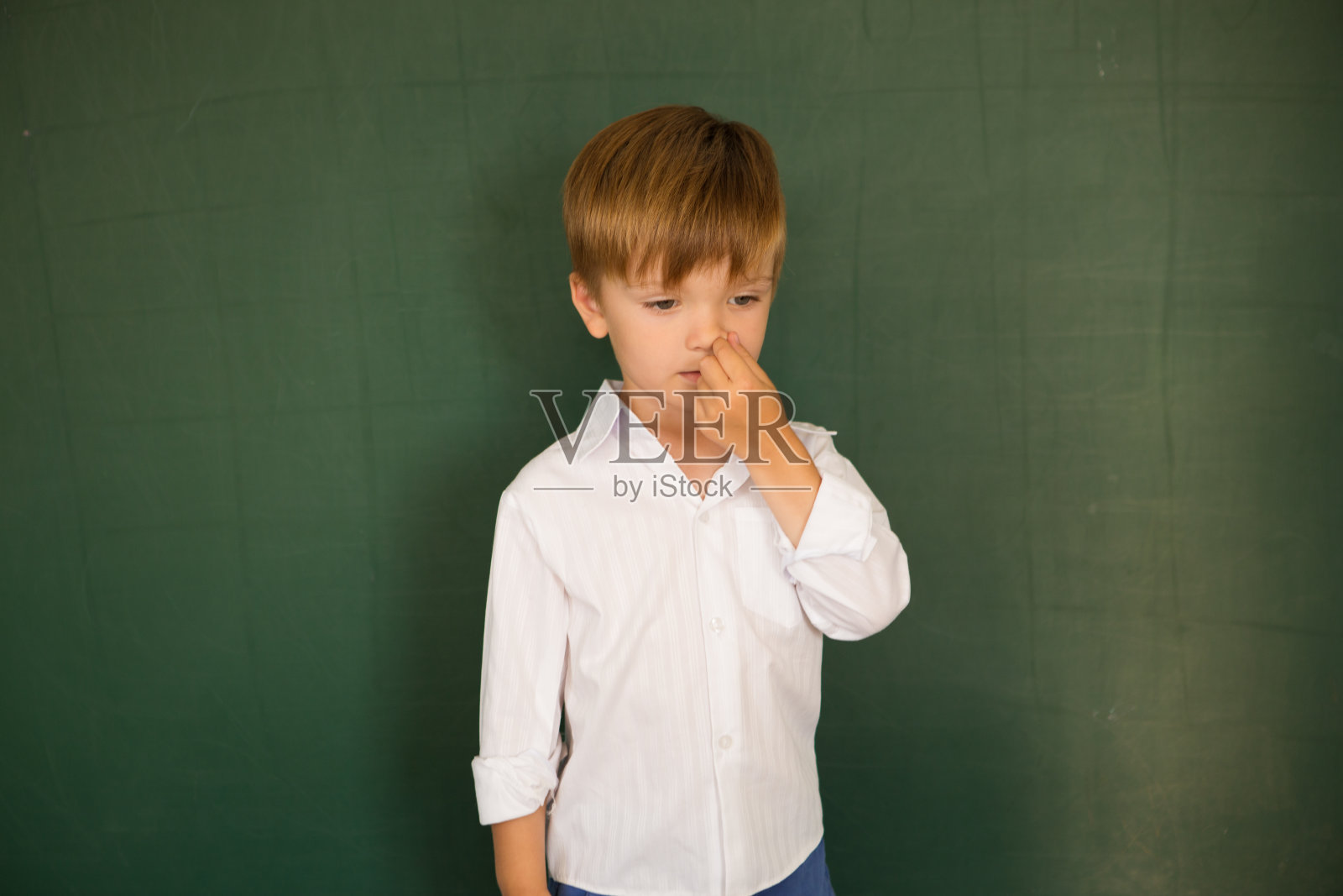 小男孩在黑板附近挖鼻子，不知道学校布置的作业的答案照片摄影图片