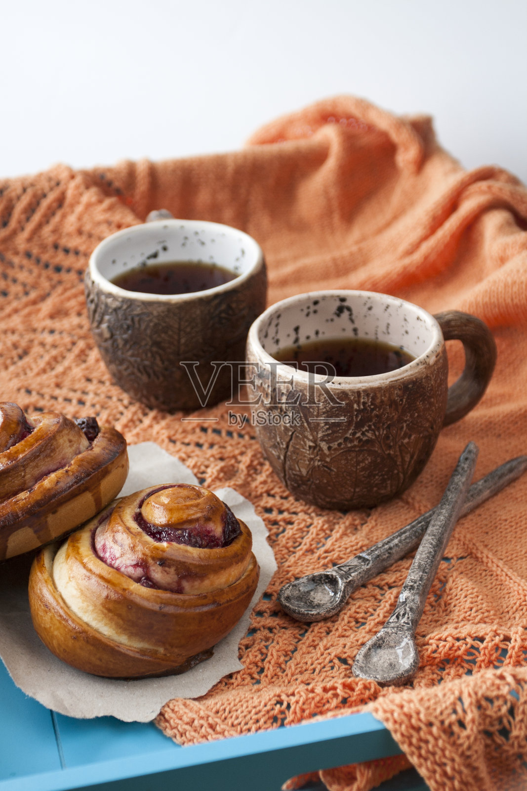 美味的果酱面包和两杯茶，蓝色木制背景。接下来是两个勺子和一个亮橙色的针织格子呢。照片摄影图片