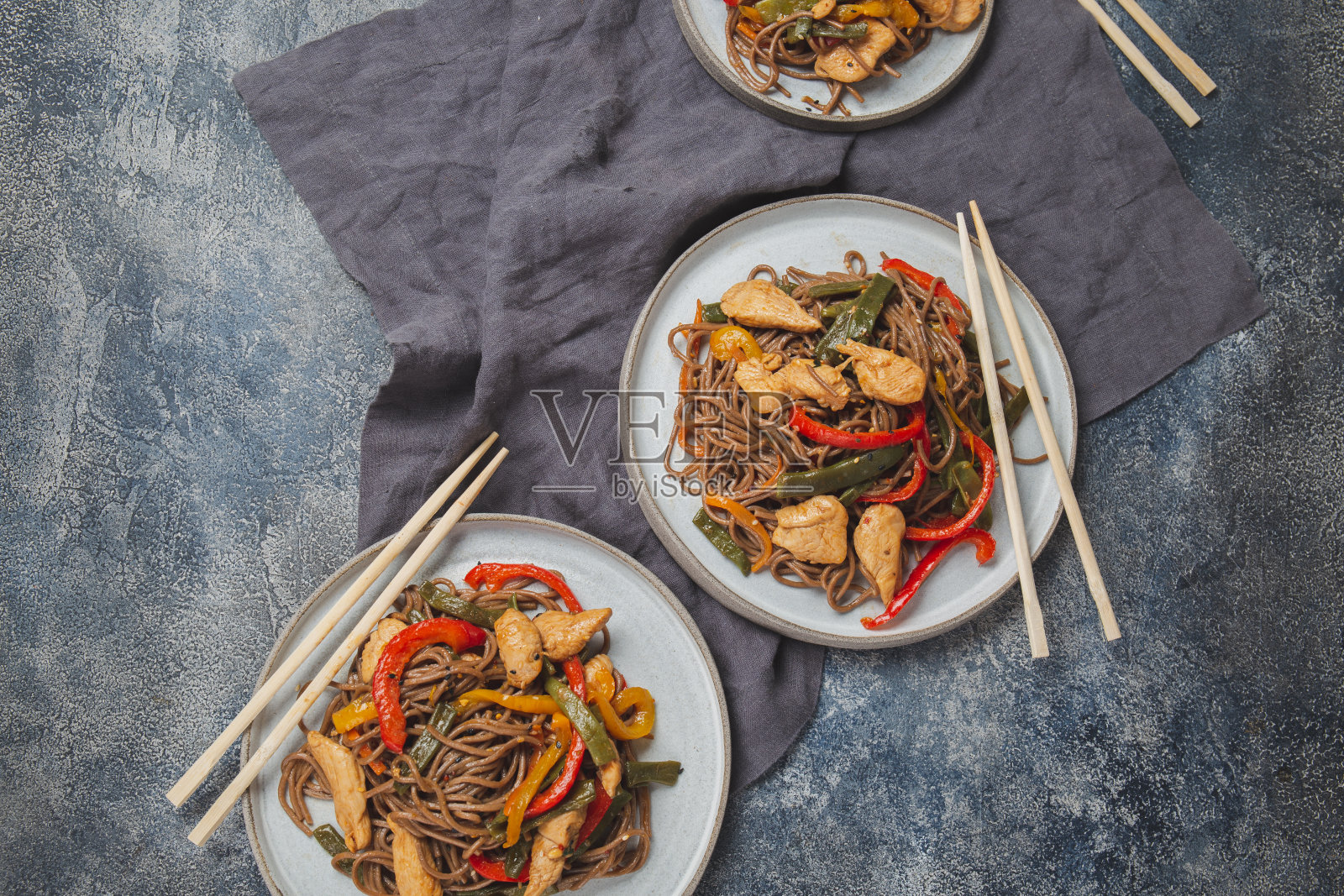 日本料理荞麦荞麦面，鸡肉和蔬菜胡萝卜，青椒和青豆，在深蓝底炒锅中照片摄影图片