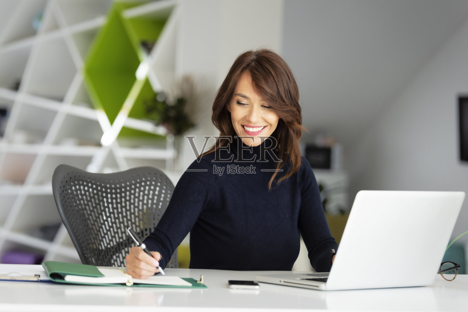 迷人的女商人穿着高领毛衣，在办公室用笔记本电脑工作照片摄影图片
