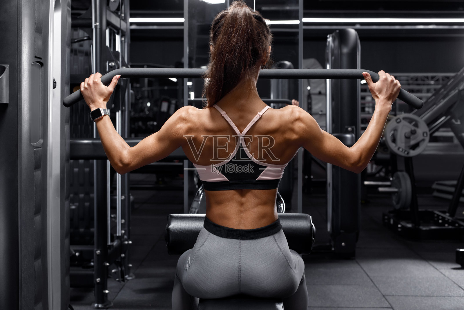 健身女在健身房锻炼背部。运动女孩做下拉照片摄影图片