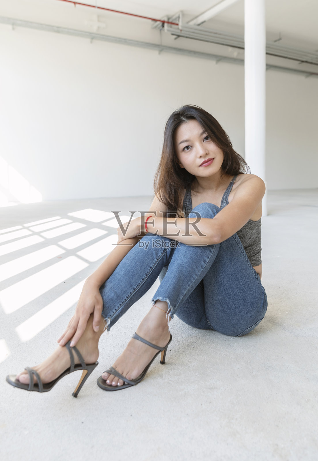 画一个漂亮的亚洲女孩坐在地上。她穿着蓝色牛仔裤、运动上衣和细高跟鞋照片摄影图片