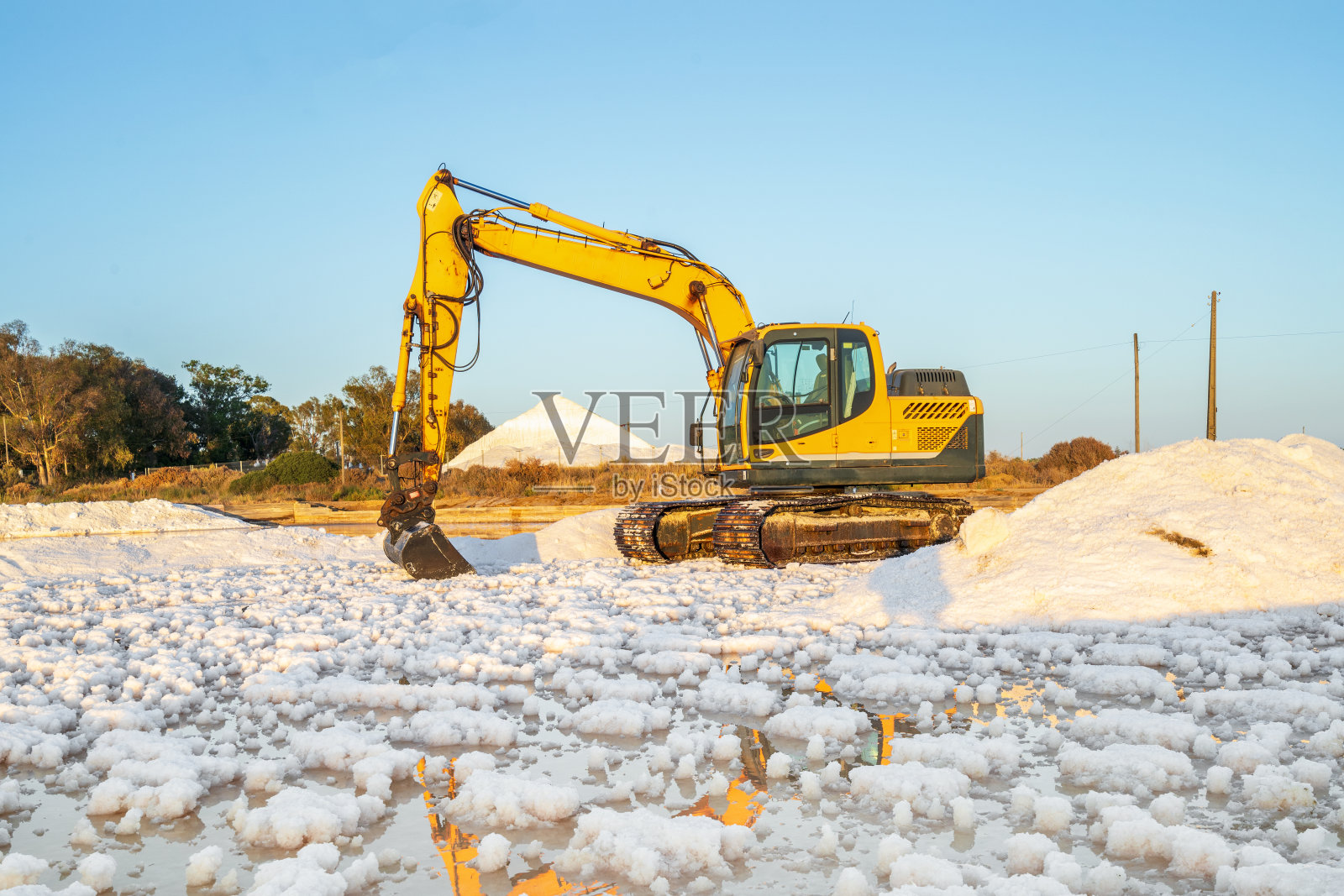 在葡萄牙法罗的盐碱地，用黄色挖掘机收获海盐照片摄影图片