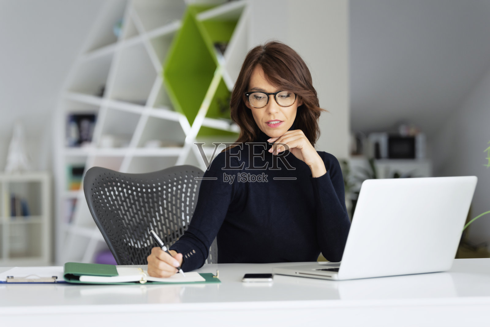 女商人穿着高领毛衣，一边在办公室用笔记本电脑写东西照片摄影图片