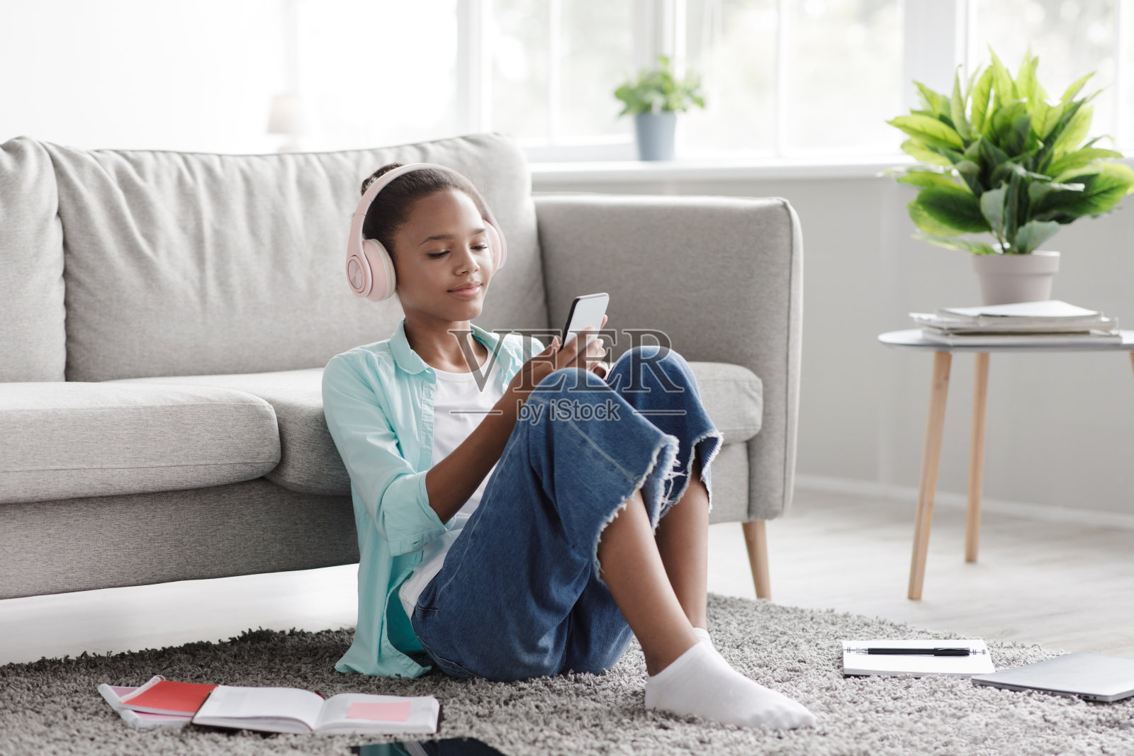 快乐的年轻黑人女孩喜欢的音乐，看视频在手机上，坐在地板上，在家里照片摄影图片