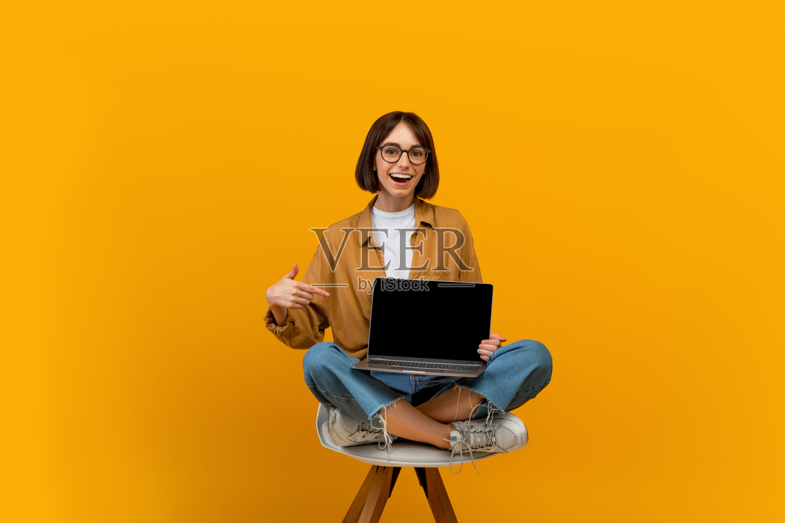 检查这个网站。快乐的女人手指着笔记本电脑黑黑的屏幕，坐在椅子上，黄色背景照片摄影图片