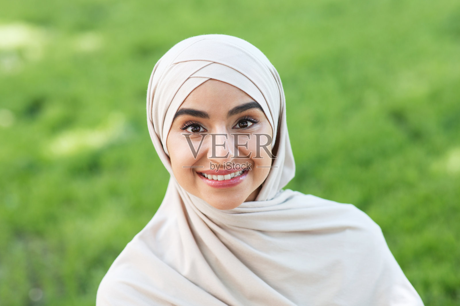 快乐迷人的千禧一代中东女性在公园里戴着头巾看着相机照片摄影图片