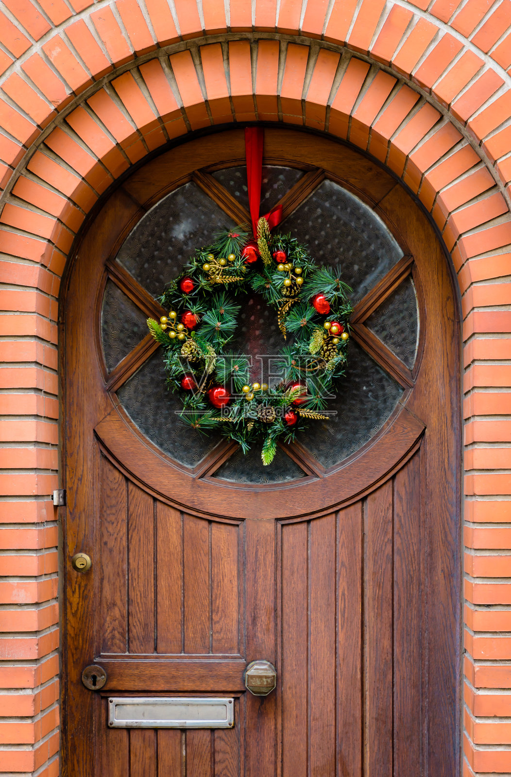 挂在有砖墙框架的木制前门上的圣诞皇冠。照片摄影图片