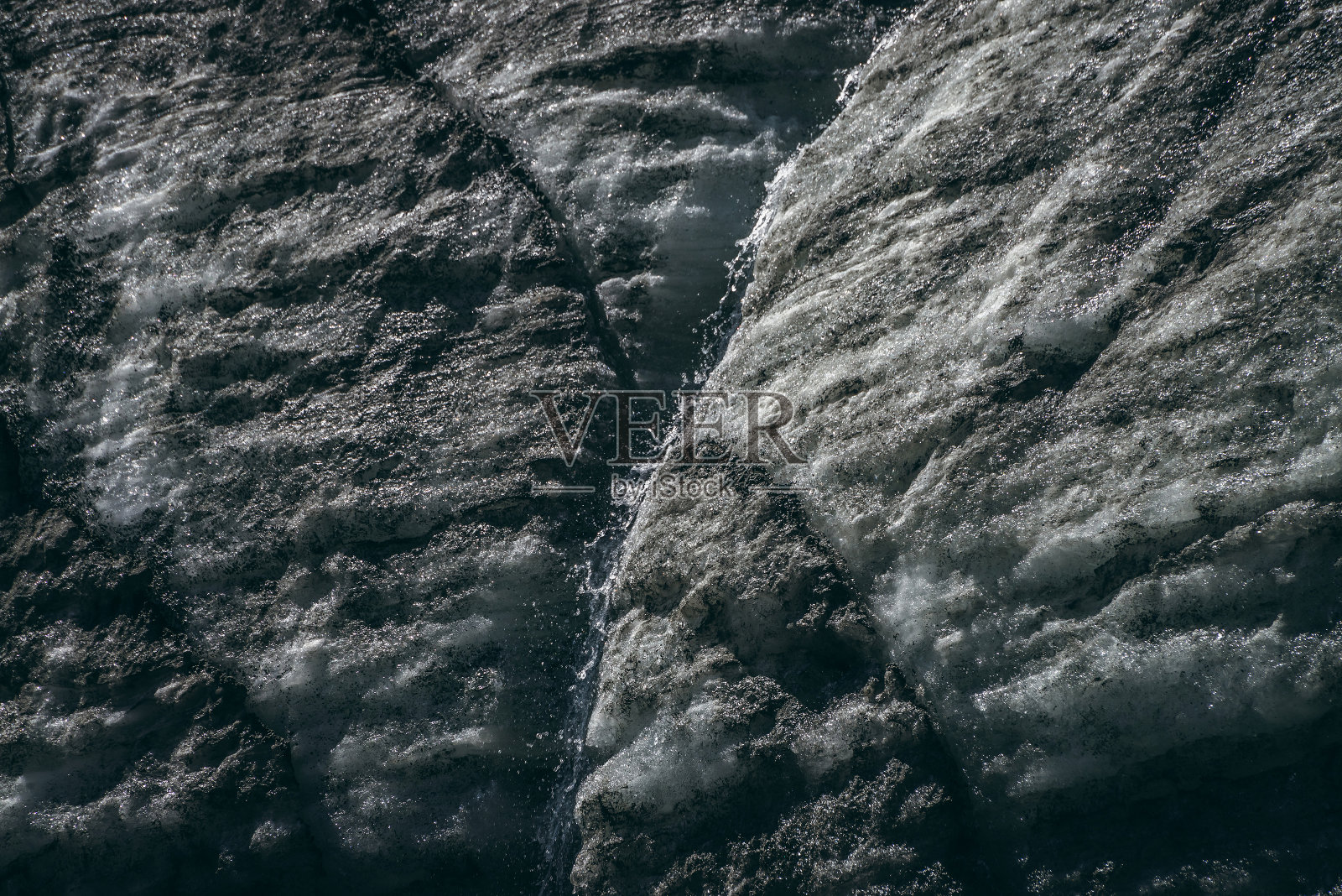 极简主义的自然背景与水流在冰川表面裂缝和划痕。最小的自然背景冰墙与小溪。闪亮的冰川表面。冰壁纹理优美。照片摄影图片