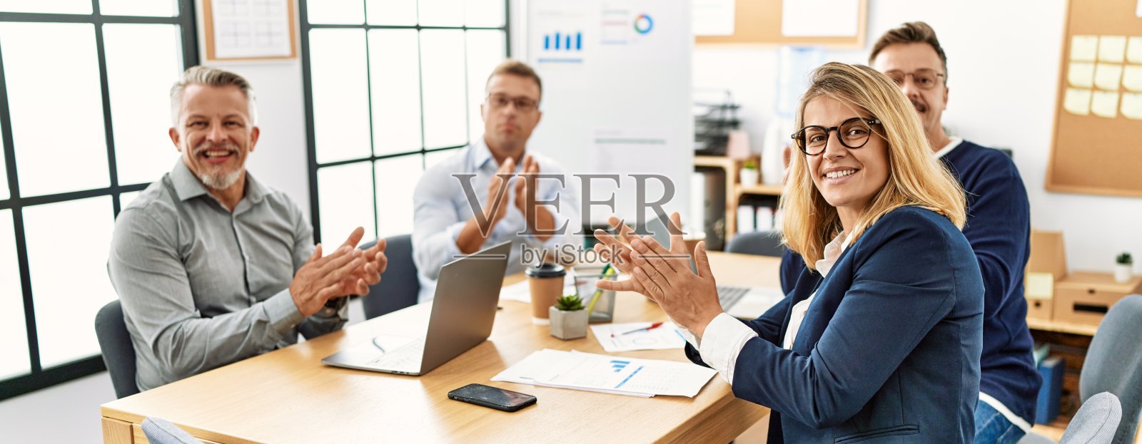 一群中年企业工人笑得开心。坐在桌子上拍手，看着办公室里的摄像机。照片摄影图片
