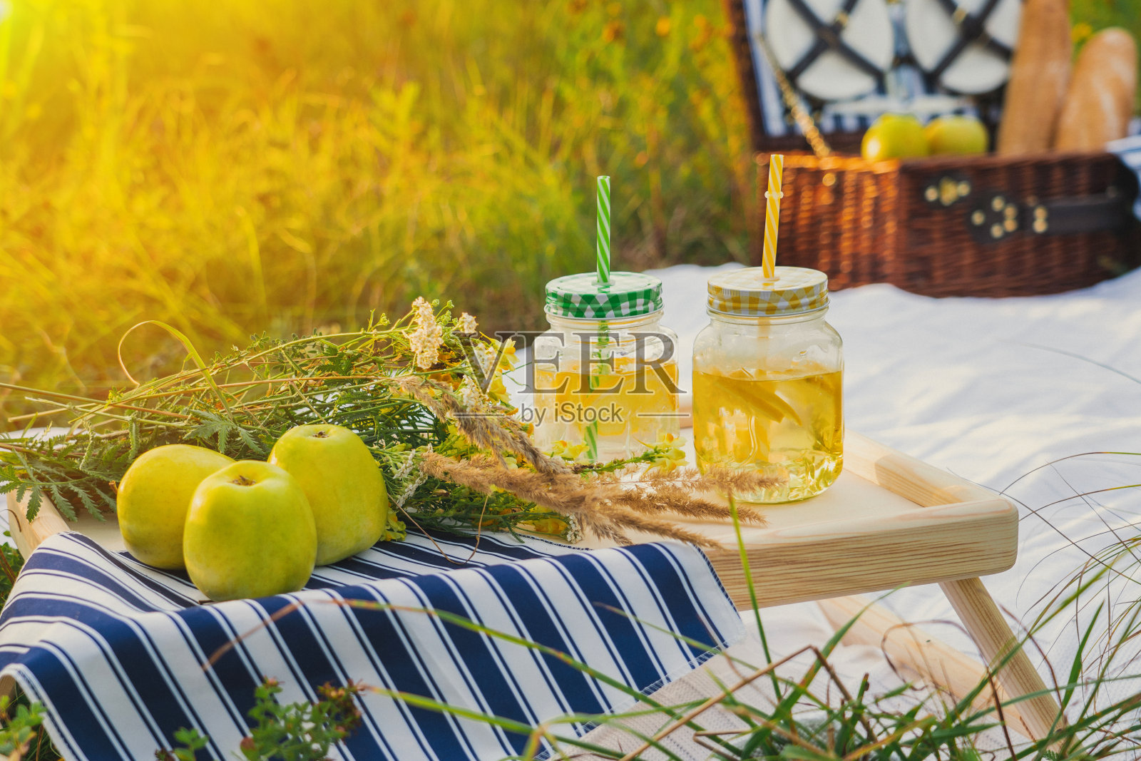 夏日日落野餐。一个漂亮的装备齐全的野餐区。一个柳条野餐盒，一条白色毯子和各种水果照片摄影图片