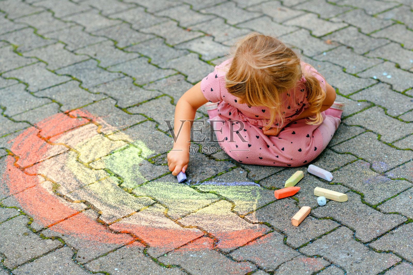 学前班的小女孩在后院的地上用彩色粉笔画彩虹。积极快乐的幼儿绘画和创作图片。夏季创造性的户外活动。照片摄影图片