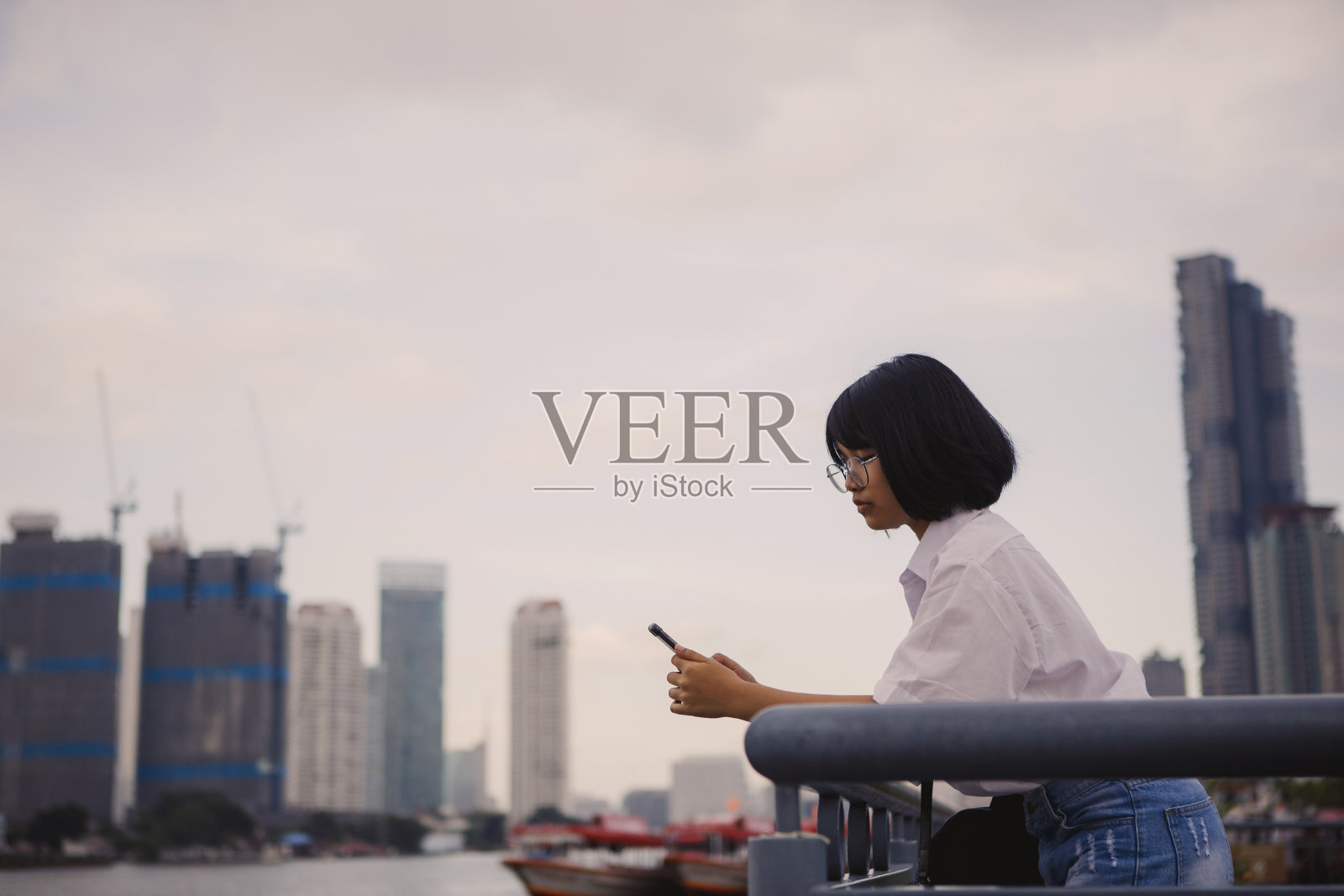 亚洲青少年阅读短信在移动电话站在城市天际线照片摄影图片