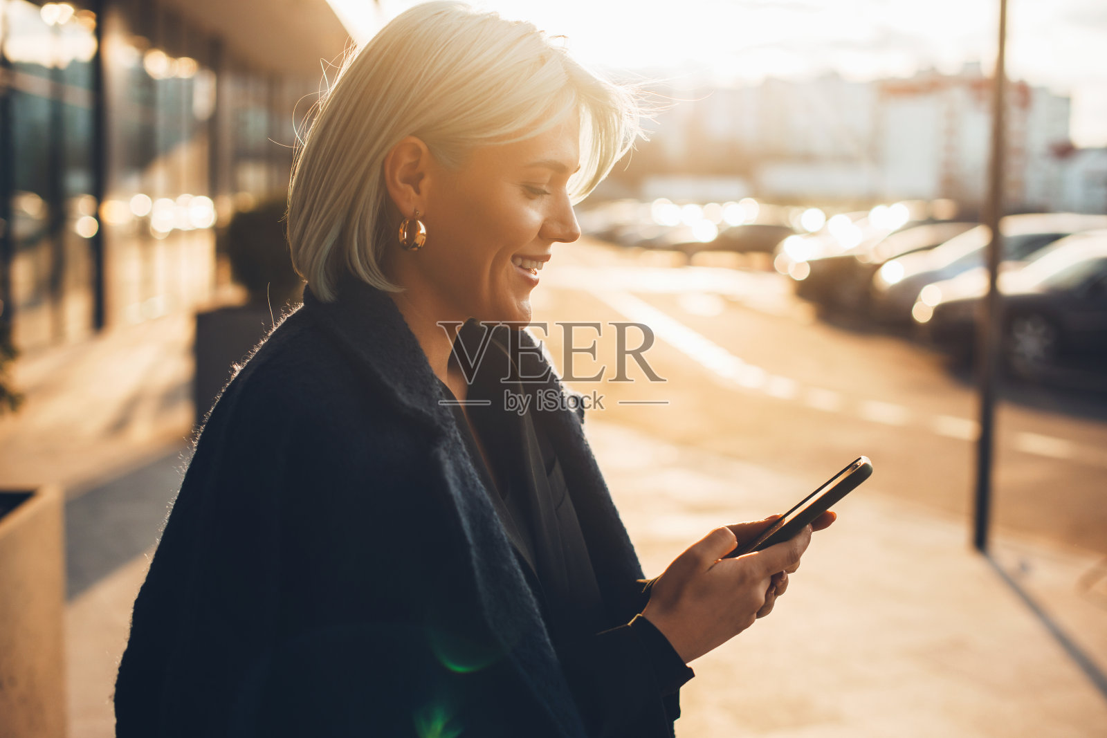一名白人女性微笑着给朋友发短信。金色的头发在夕阳下。年轻女子收到一些好消息在她的手机和微笑照片摄影图片