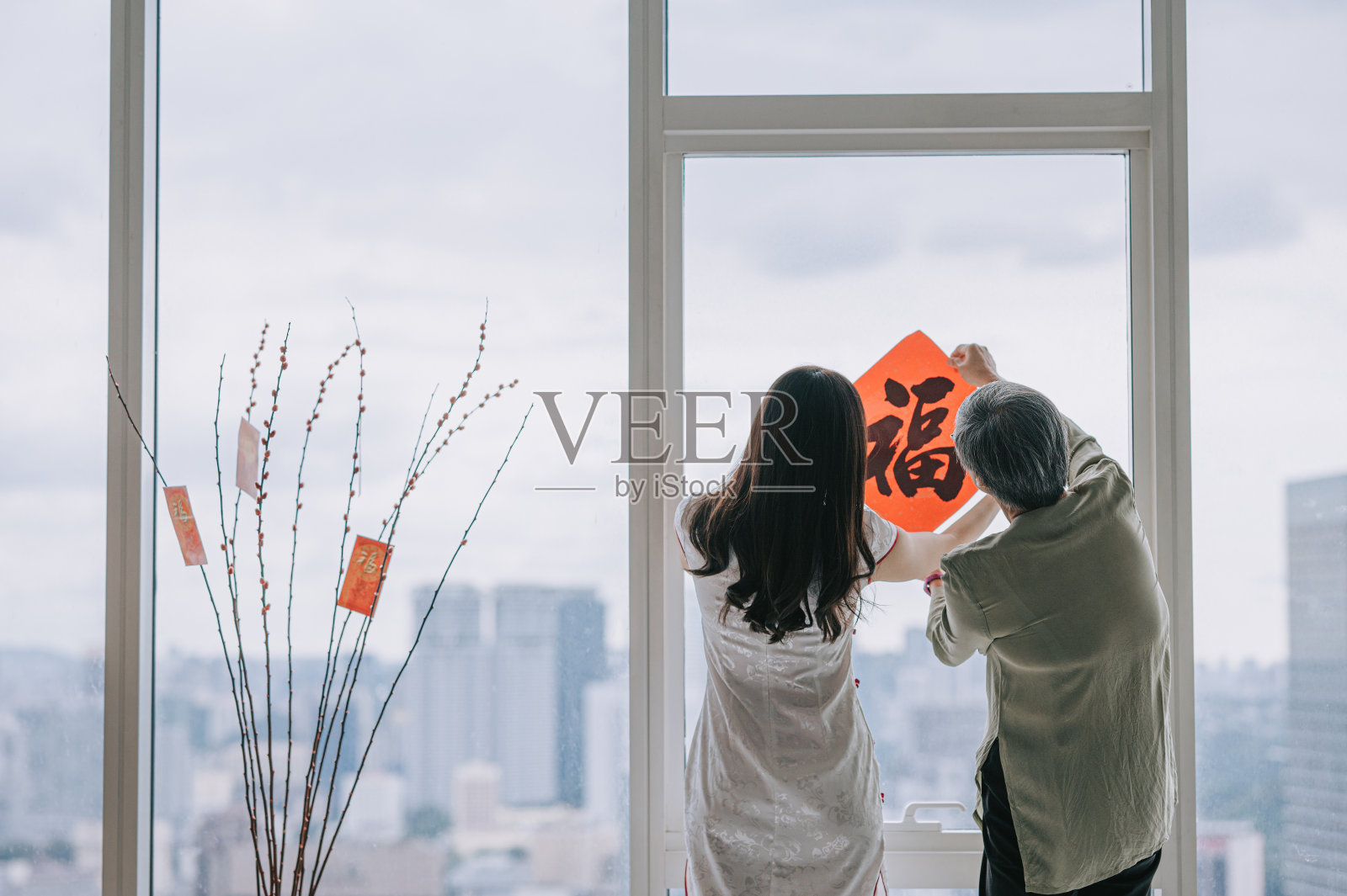 后视图中国新年妇女和她的女儿装饰房子的客厅与中国书法装饰的窗户准备家庭团聚照片摄影图片