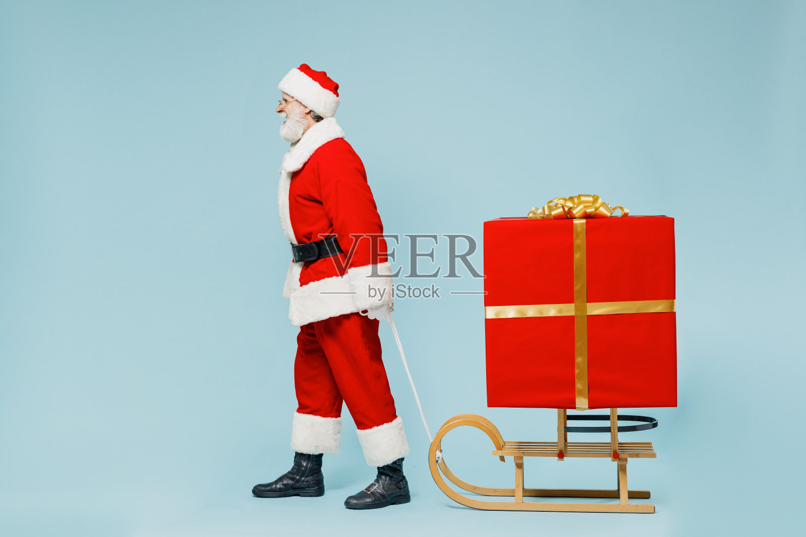 全身都是圣诞老人，戴着圣诞帽，穿着红色西装，拉着雪橇，带着大礼盒，被隔离在纯蓝色背景的工作室里。2022年新年快乐庆典，圣诞快乐节日概念。照片摄影图片