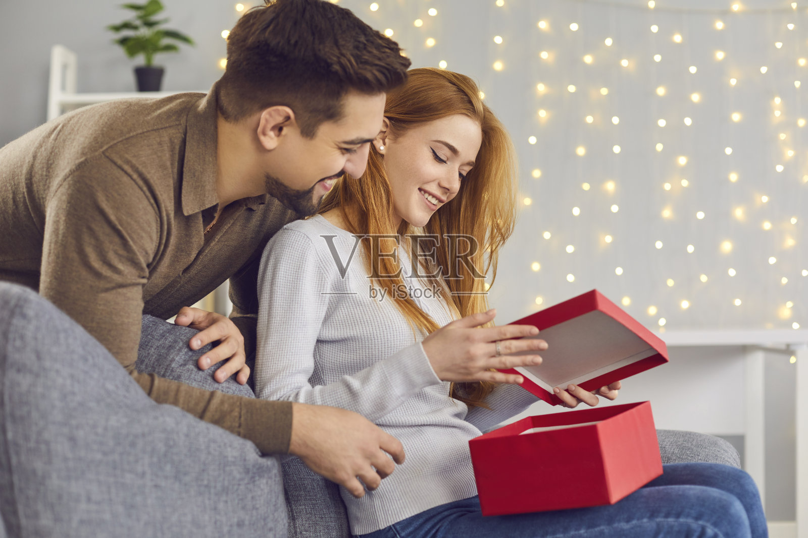 快乐的年轻女子坐在沙发上，打开男友送的情人节礼物照片摄影图片