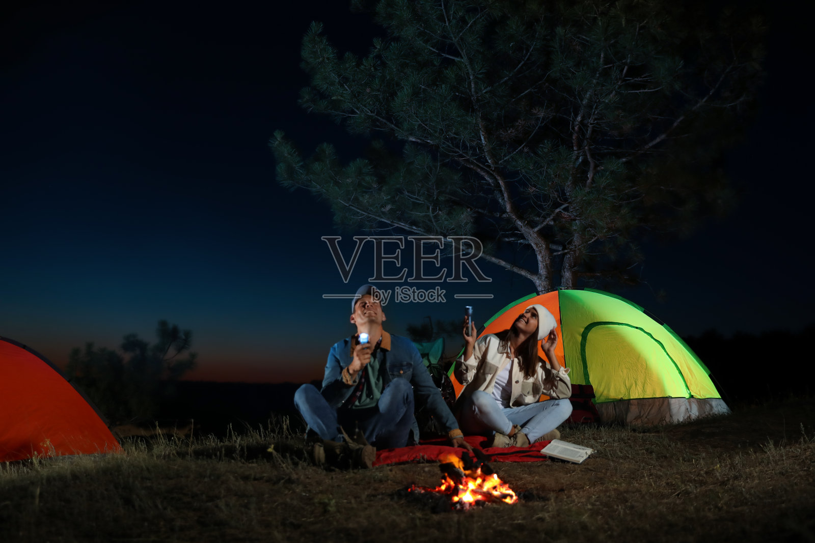 一对晚上在篝火旁打着手电筒的夫妇。露营的季节照片摄影图片
