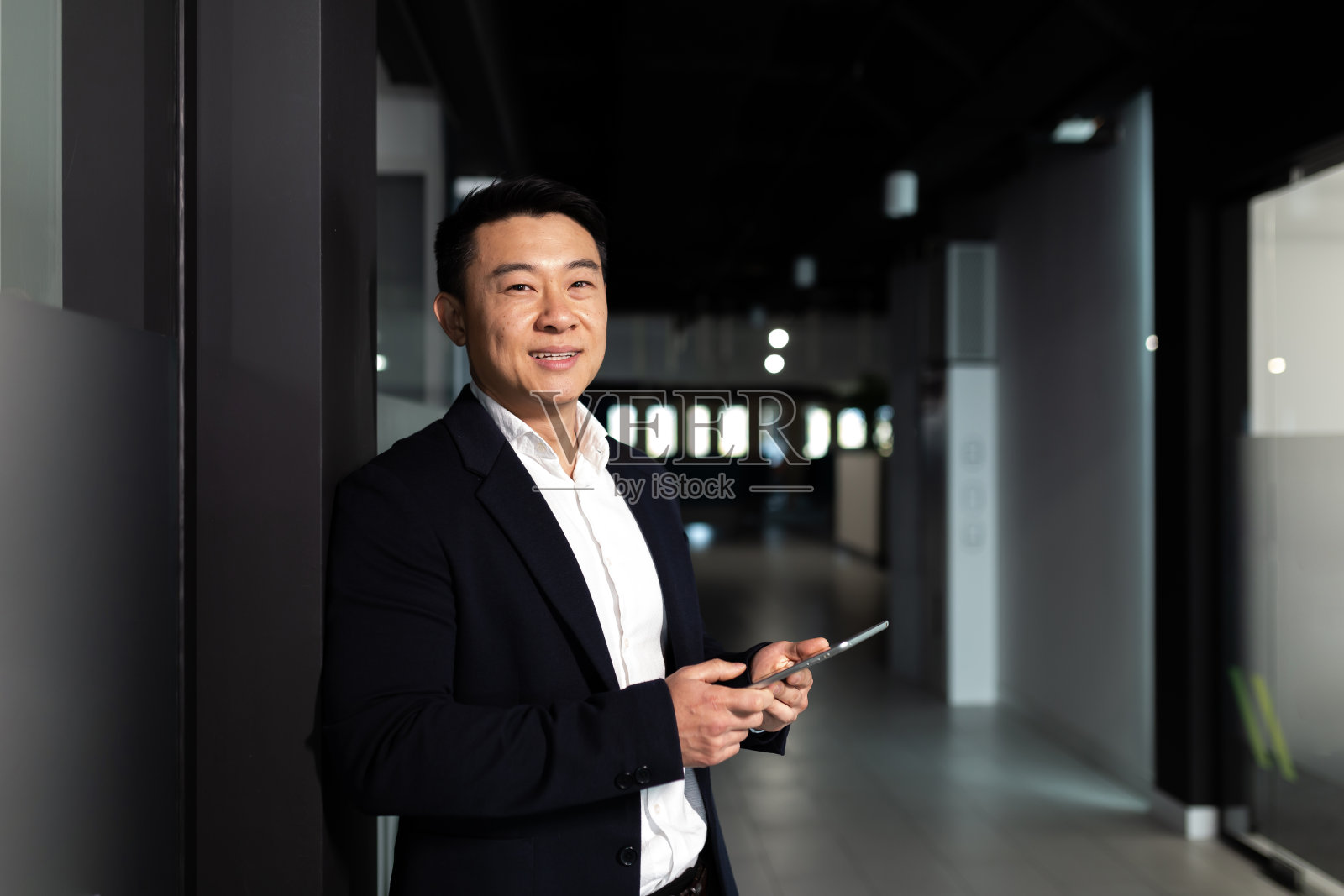 成功的亚洲商人老板，穿着西装，面带微笑，使用平板电脑，在一间现代化的办公室里工作照片摄影图片