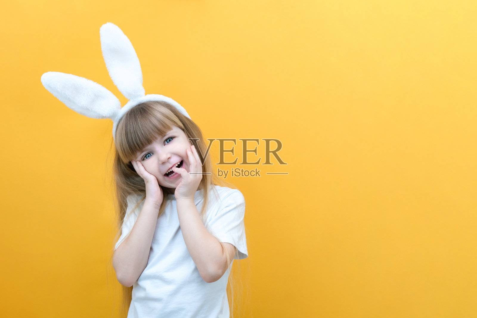 黄色的背景上，头上戴着兔耳朵的快乐女孩。有趣疯狂快乐的孩子。复活节的孩子。为复活节假期做准备。促销产品。本空间照片摄影图片