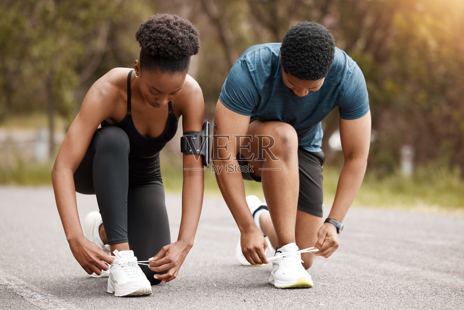 一对健康的非洲裔美国夫妇在户外跑步前系鞋带。年轻的男女运动员训练，以提高他们的有氧和耐力，以保持健康的生活方式。他们喜欢一起锻炼照片摄影图片