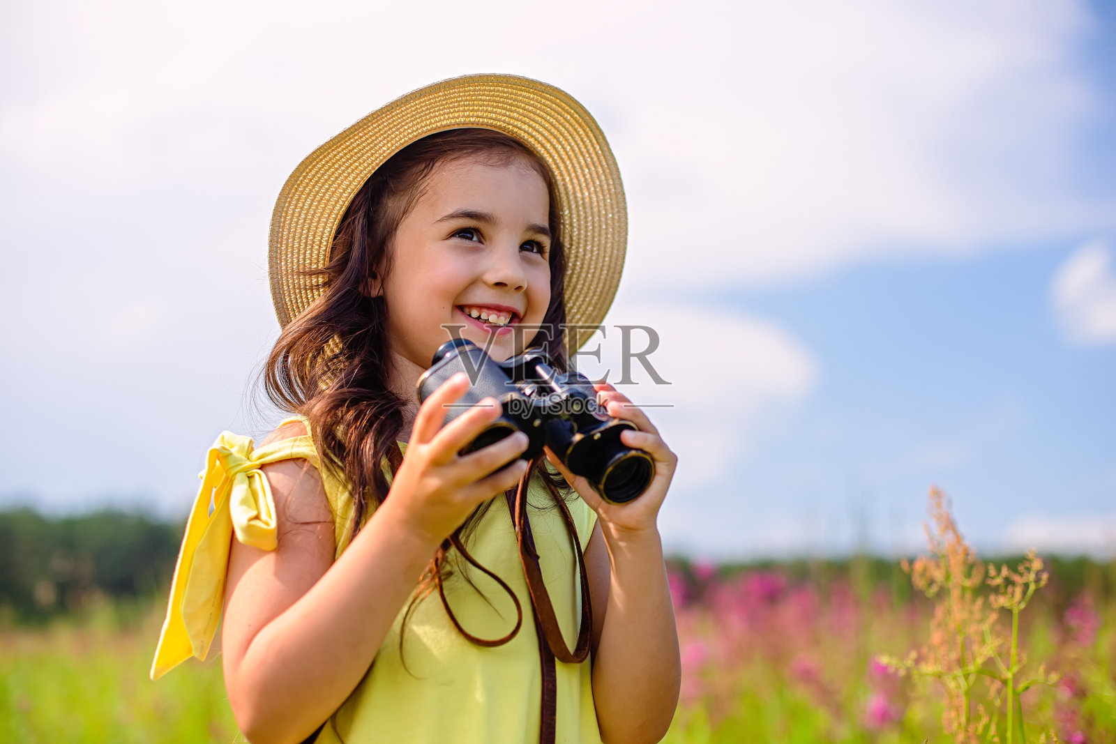 可爱的女孩戴着草帽，站在蓝天下高高的草地上，拿着望远镜照片摄影图片