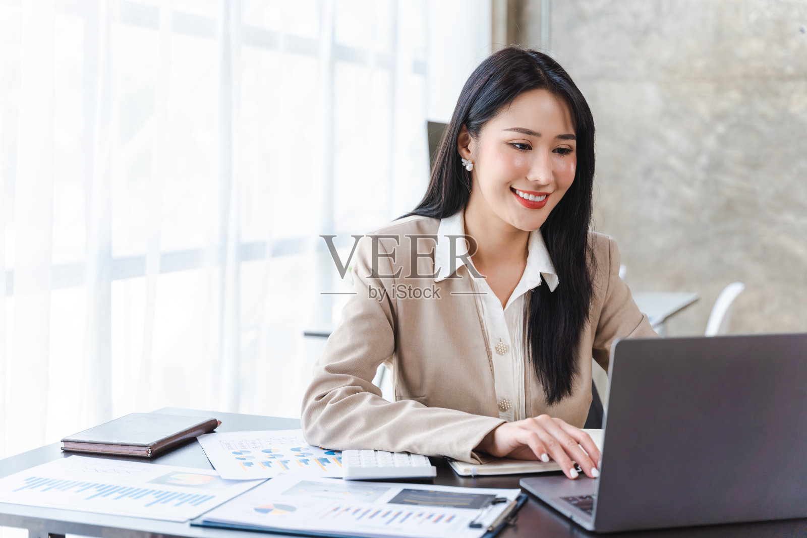自信快乐的年轻女性在她的办公室里用笔记本电脑工作。美容亚洲商业女性的概念。照片摄影图片