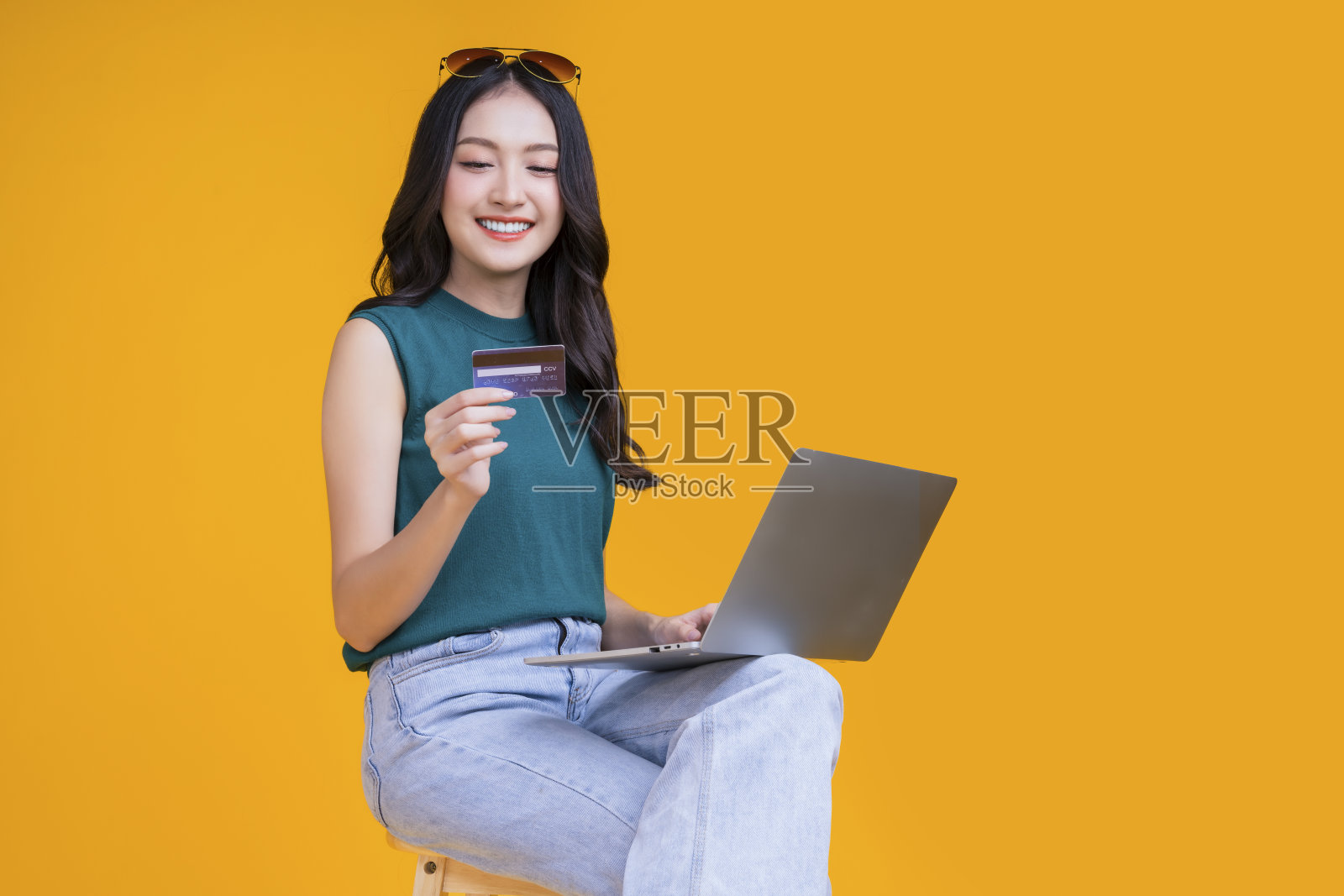 聪明的亚洲女性用信用卡手提电脑微笑着自信开朗的工作室拍摄，亚洲年轻成年女性坐在凳子上的手势持有信用卡护理无现金支付业务的想法照片摄影图片