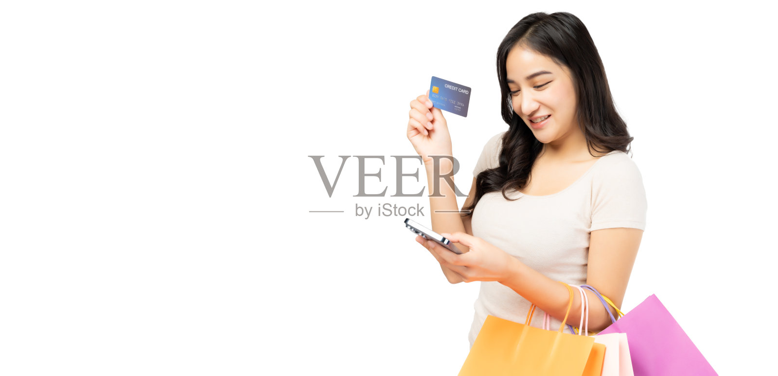 年轻的亚洲女士使用手机手持信用卡携带购物袋孤立的白色背景和复制空间微笑的年轻女孩通过手机购买使用信用卡享受购物照片摄影图片